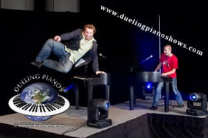 Two men performing at a dueling piano show on stage.