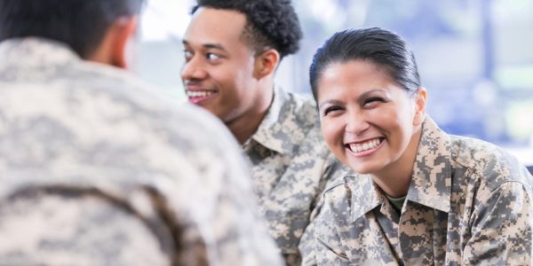 Smiling soldiers in camouflage uniforms having a conversation indoors.