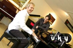 Two musicians playing a piano in a music studio setting.