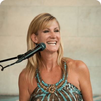 A woman smiling while playing the piano and singing into a microphone.